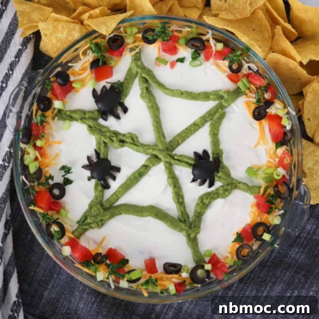 A visually stunning spider web bean dip, perfectly crafted for Halloween menus, featuring intricate guacamole web patterns and olive spiders.