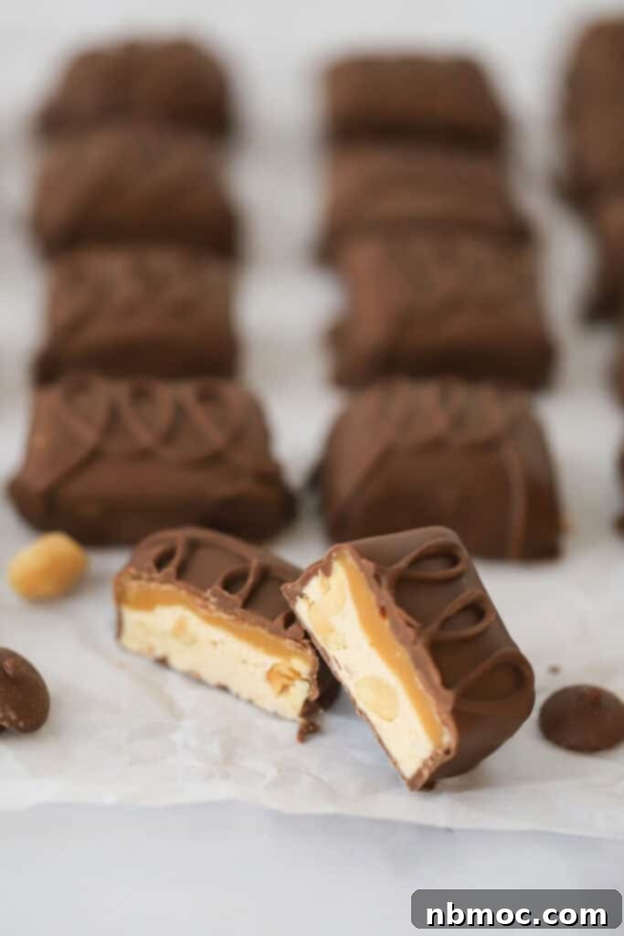 Mini homemade snickers candy bars on a baking sheet with one cut in half so you can see the layers.