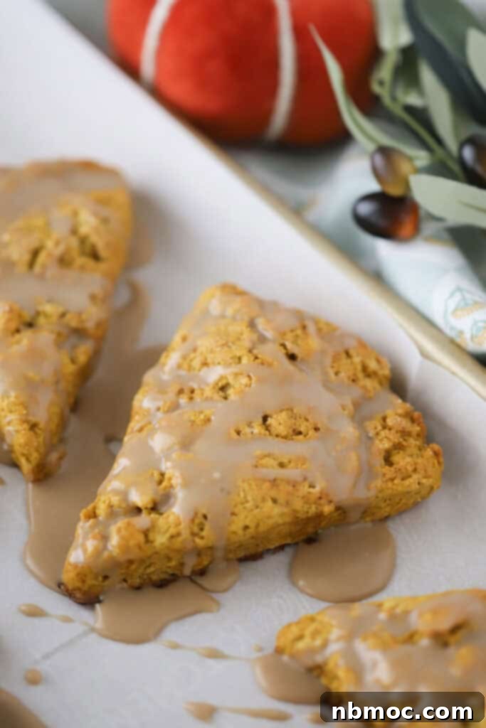 A baking sheet with two freshly baked pumpkin scones, beautifully topped with a glistening maple syrup glaze, ready to be enjoyed.