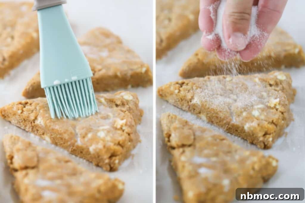 A hand brushing milk over the tops of unbaked pumpkin scones before sprinkling them with sugar, ready for the oven.