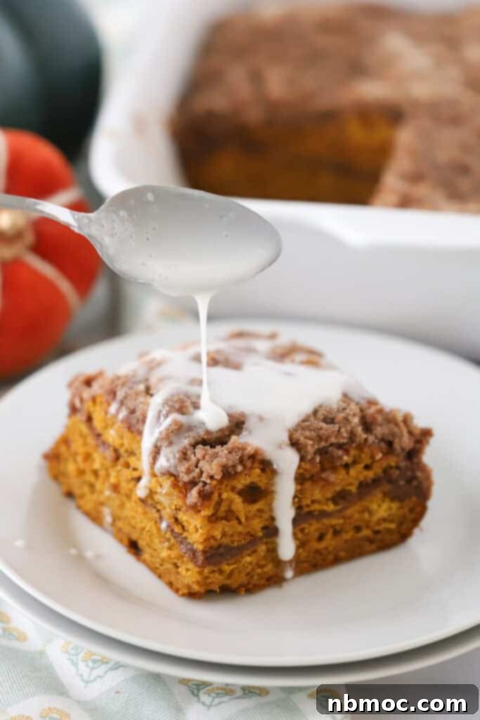 Pumpkin crumb cake on a white plate with a spoon that is drizzling glaze over the top.
