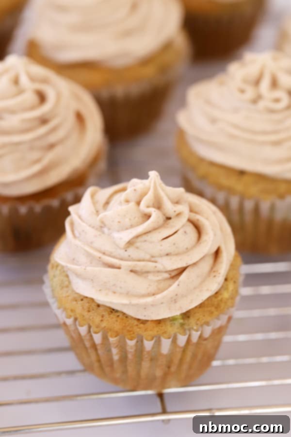 Sweet Zucchini Gems 2 Healthy zucchini cupcakes topped with cinnamon buttercream frosting on a wire cooling rack.