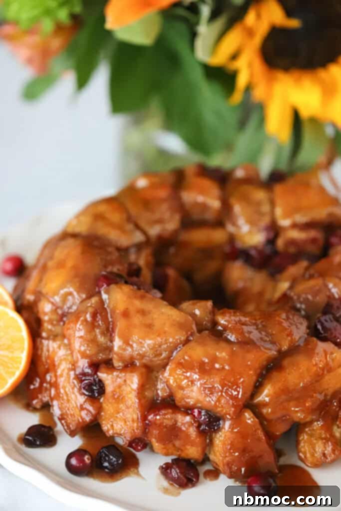 Zesty Cranberry Orange Pull-Apart Delight 2 A white serving plate with cranberry orange monkey bread covered in caramel sauce.