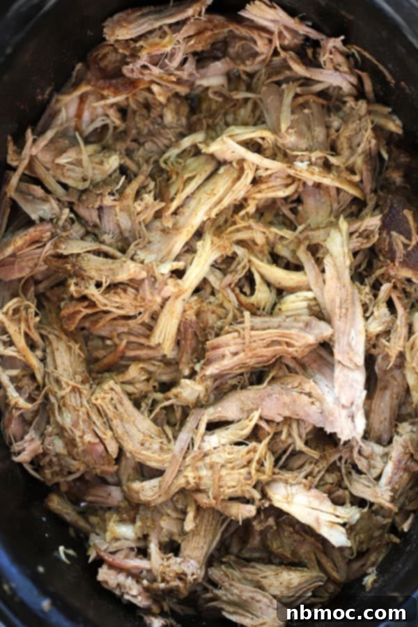 Shredded pork picnic roast slow cooker, easy crock pot picnic roast. A serving of juicy pulled pork on a bun with coleslaw and a pickle.