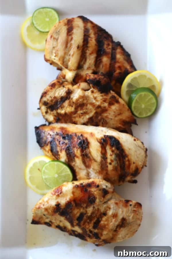 Perfectly grilled citrus chicken breasts arranged on a white serving platter, garnished with fresh lime and lemon slices. A delectable chicken marinade with orange juice delivers this flavorful meal.