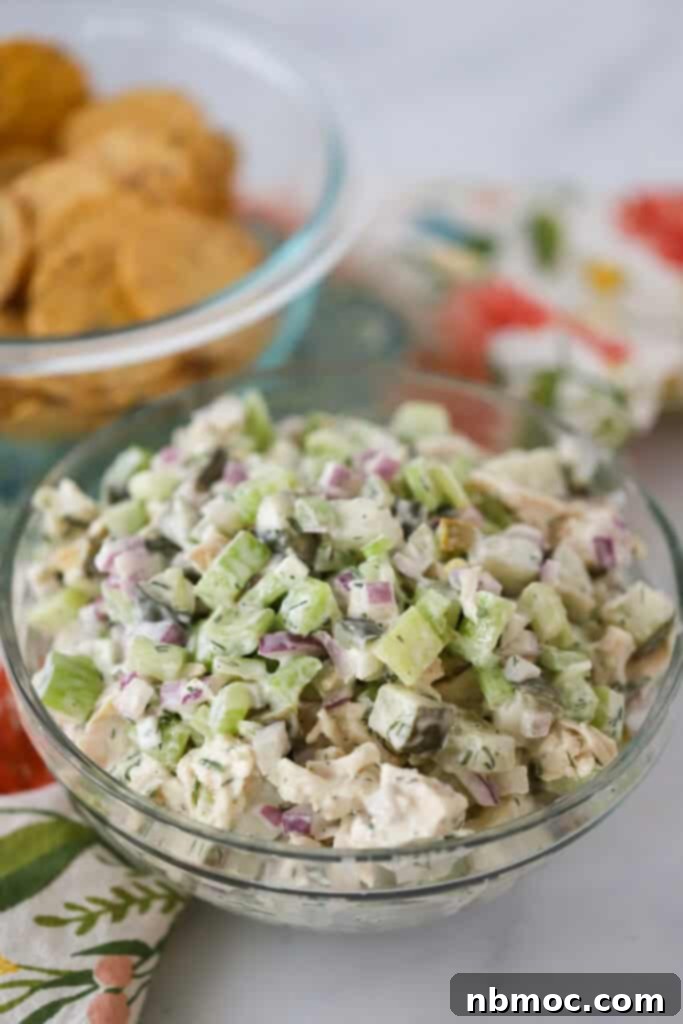 A glass bowl full of dill pickle chicken salad. pickles chicken salad in a clear glass bowl. 