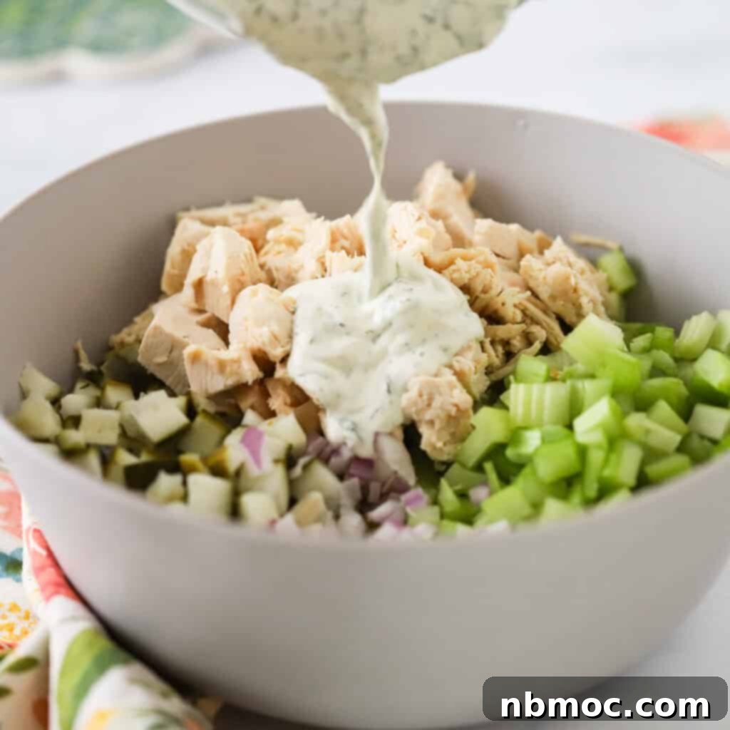 A large white bowl full of dill pickle chicken salad ingredients with dill pickle dressing being poured over the top.