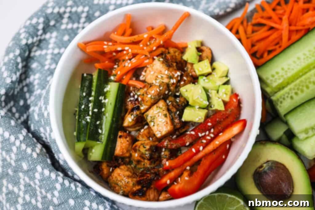 A honey soy salmon bowl on a table filled with fresh sliced veggies, avocado, and topped with sesame seeds.