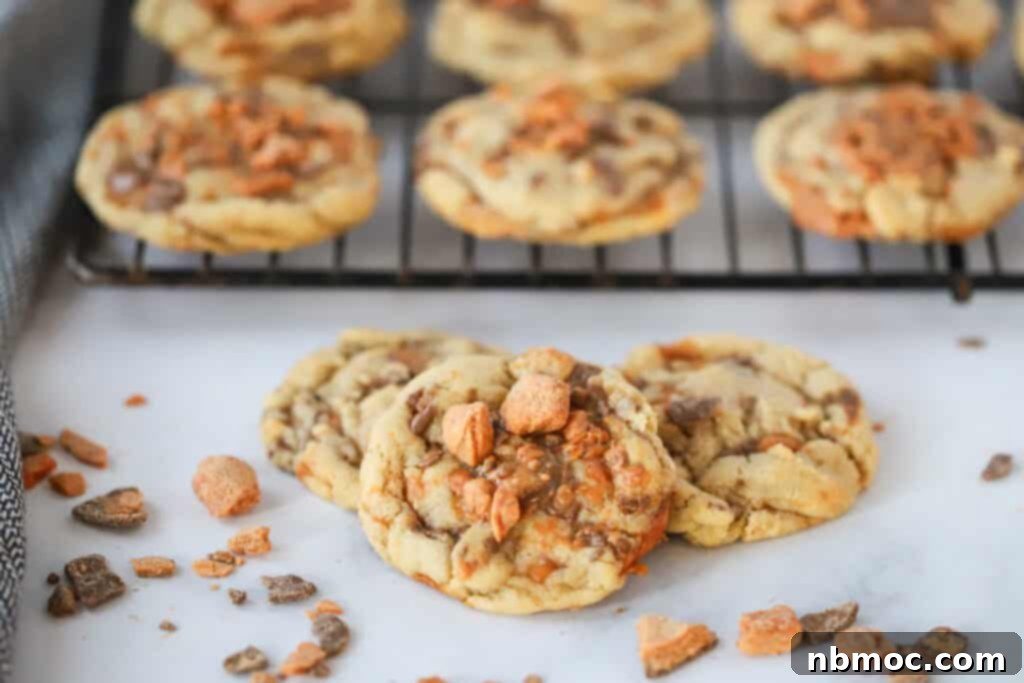 A stack of cookies made using this butterfinger cookie recipe, with some cooling on a wire rack behind.