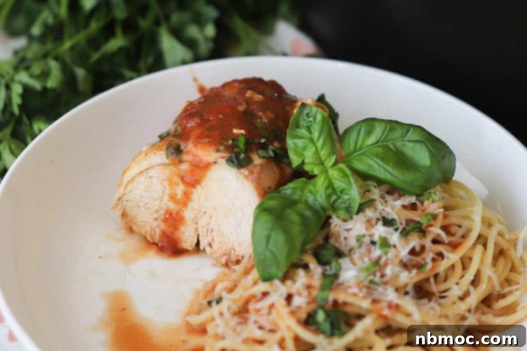 A white plate with crock pot chicken Parmesan and a side of spaghetti topped with basil. 