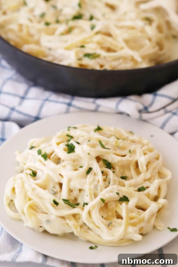 Quick Creamy Alfredo 2 Homemade Alfredo sauce with heavy cream and chicken broth, generously covering fettuccine noodles in a rustic setting.