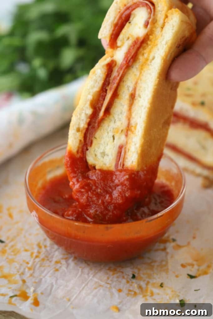 A hand dipping a slice of stromboli into marinara sauce.