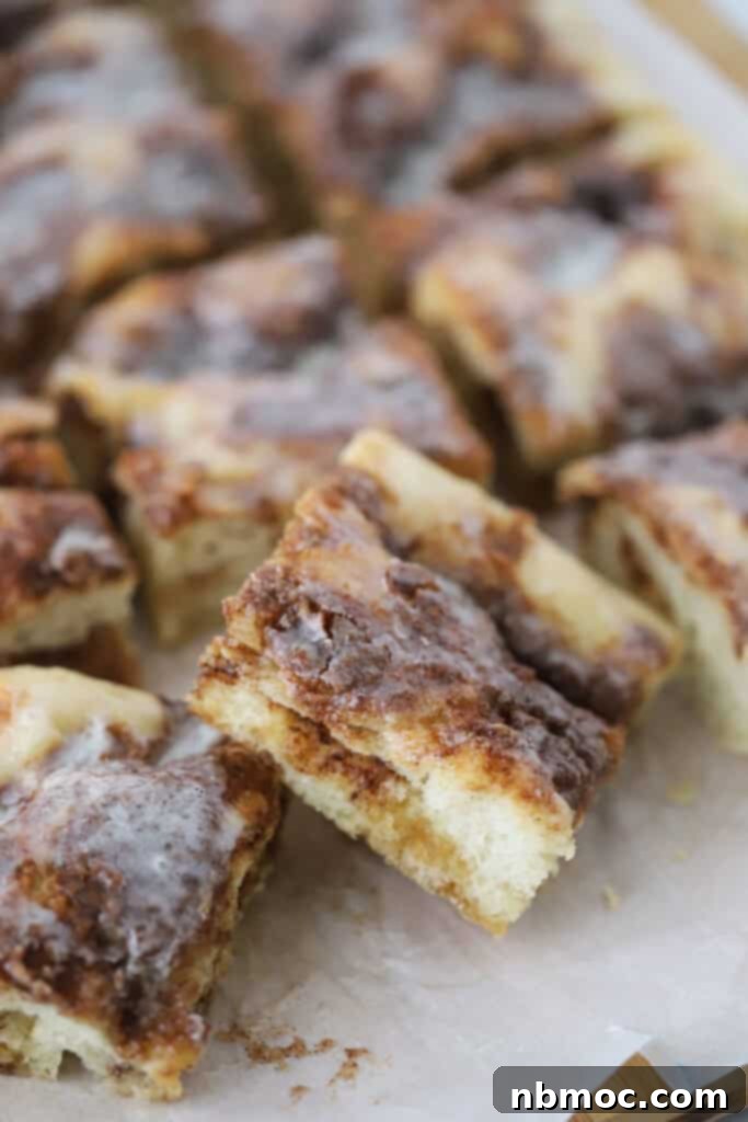 Squares of cinnamon roll dessert focaccia on a cutting board, topped with sweet icing.