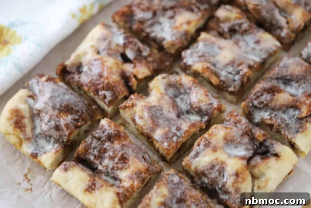 Cinnamon focaccia cut into pieces on a cutting board, generously covered with sweet glaze.