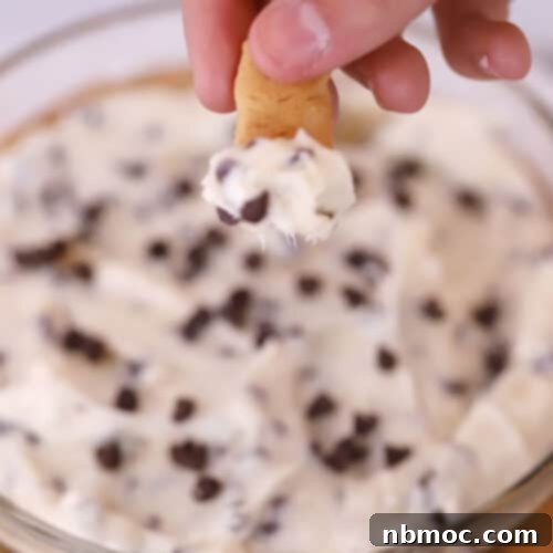Chocolate chip cheesecake dip in a clear bowl with a graham cracker being dipped.