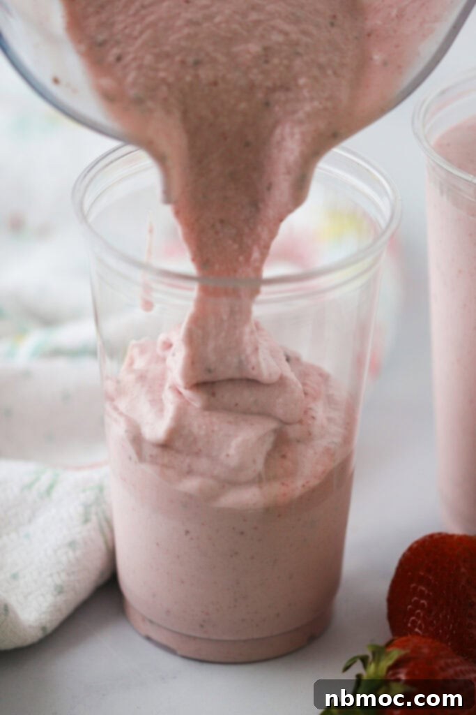 Pouring a vibrant strawberry and banana smoothie into a clear plastic cup.
