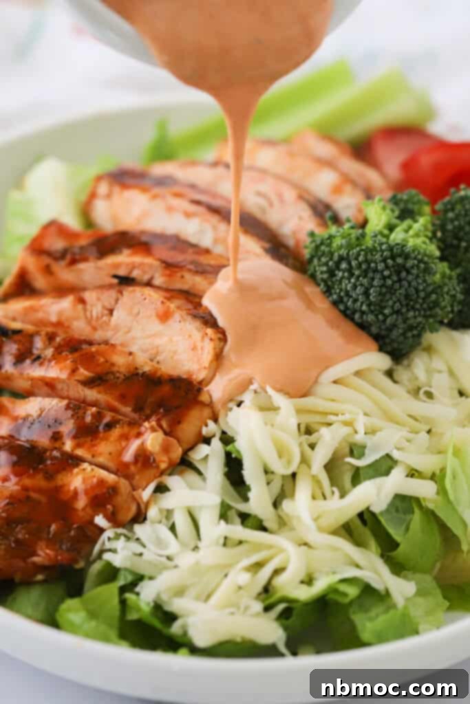 Bold Buffalo Chicken Salad 4 Buffalo ranch dressing being poured over the top of a grilled chicken salad.