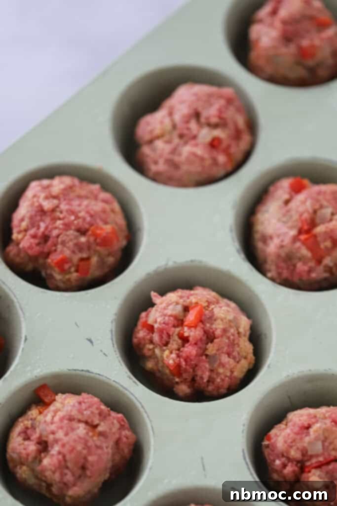 Unbaked meatloaf mixture, perfectly portioned and pressed into the cups of a muffin pan, awaiting the oven.