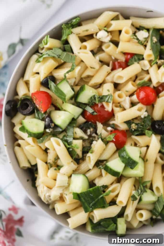 Santorini Sunset Pasta Salad 2 A big serving bowl full of this Greek Pasta Salad with feta, tomatoes, cucumbers, and olives. The salad is colorful and inviting, ready to be served.