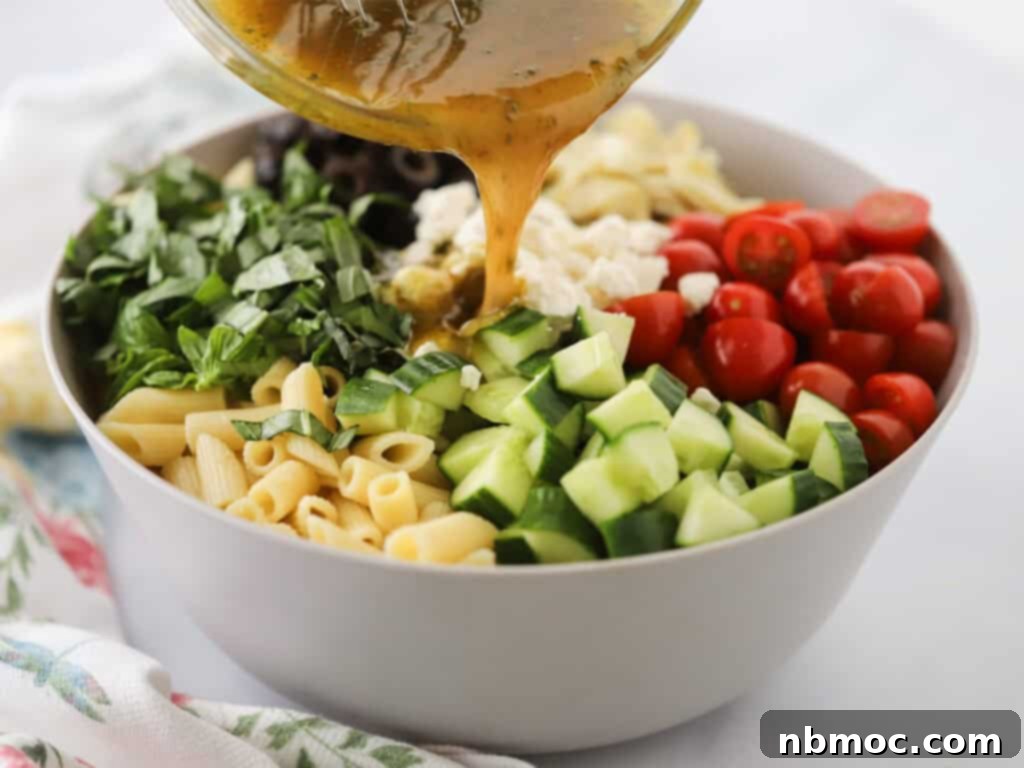 Santorini Sunset Pasta Salad 4 Pouring dressing over Greek pasta salad ingredients in a large mixing bowl.
