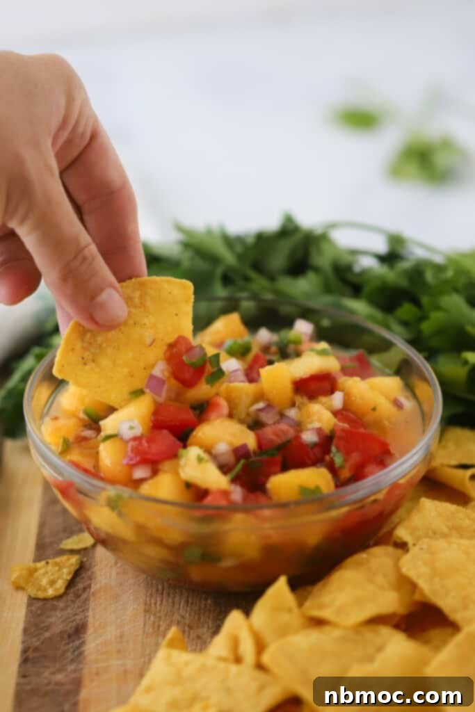 A hand holding a chip and dipping it into peach salsa, showcasing its chunky texture and vibrant colors.