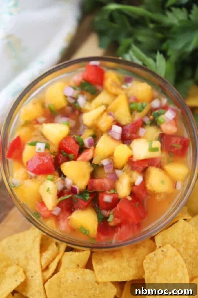 A small glass bowl full of vibrant tomato peach salsa topped with red onions and fresh cilantro leaves.
