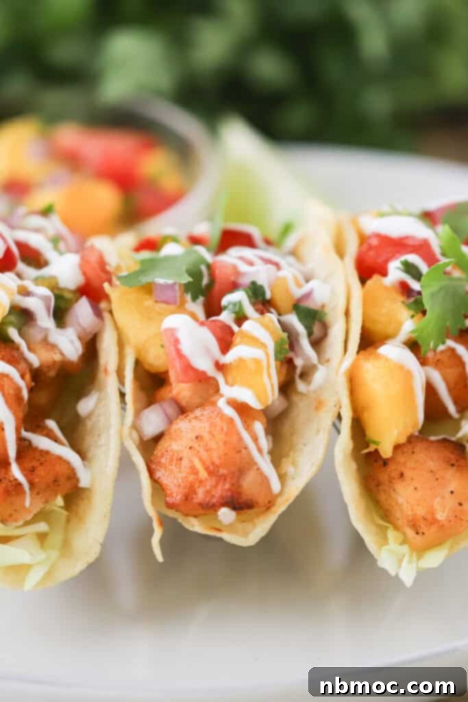 Two perfectly assembled air-fried fish tacos, generously filled with golden salmon bites, vibrant peach salsa, and a luscious drizzle of lime crema, ready to be enjoyed.