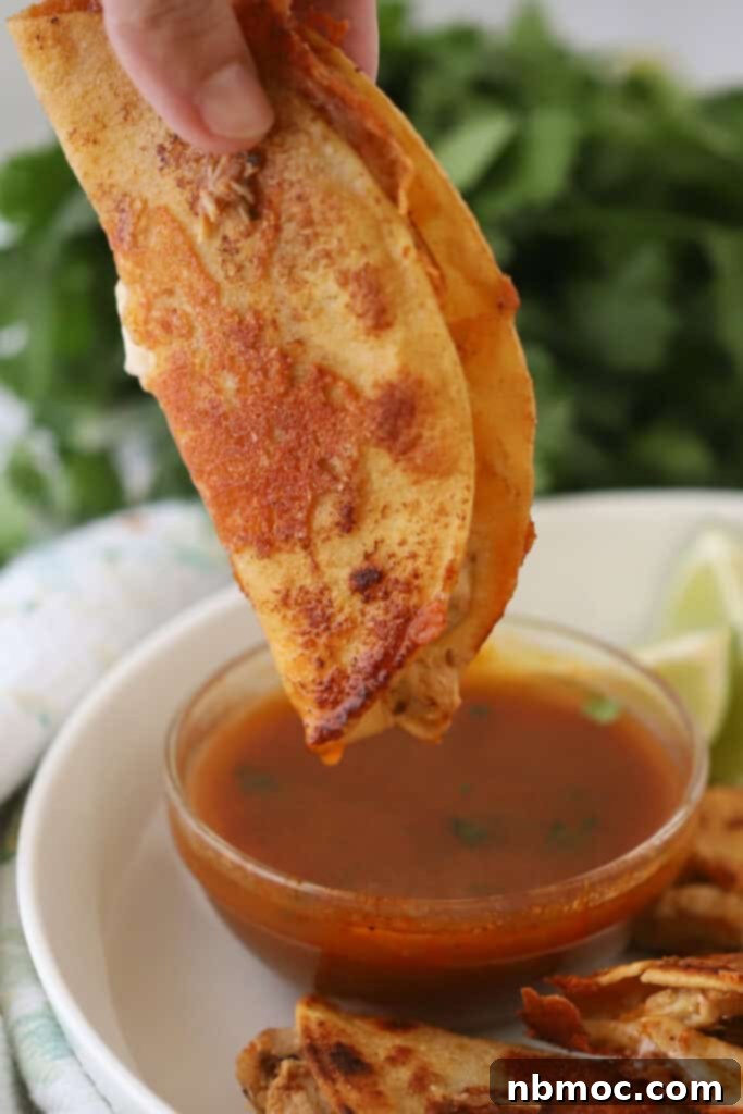 Mouthwatering Chicken Birria Tacos 2 A hand dipping a chicken birria taco into sauce.