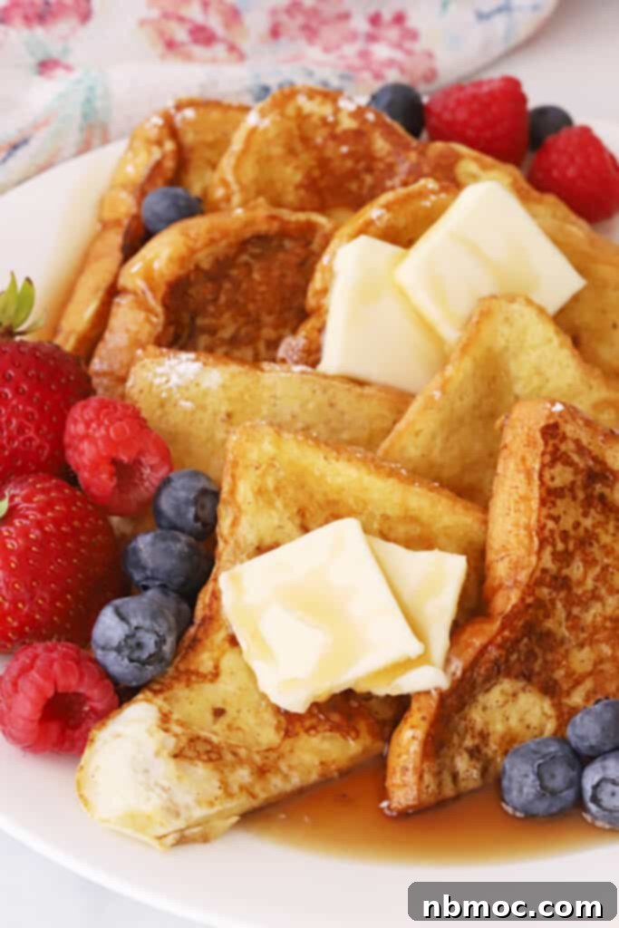 Classic french toast recipe, stacked on a plate with berries, butter and syrup.