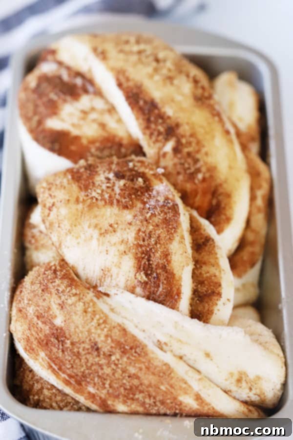 Close-up of a golden-brown cinnamon swirl bread baking in a loaf pan, showing its intricate twisted pattern.