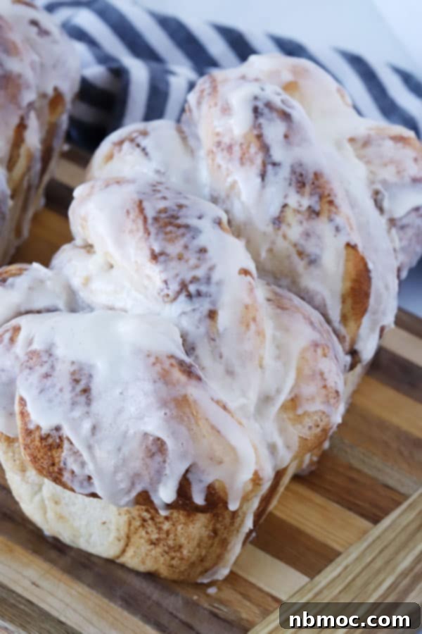 A freshly baked Cinnamon Twist Bread, generously drizzled with white icing, resting on a wooden cutting board.