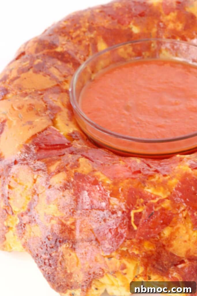 A freshly baked Pizza Monkey Bread, inverted onto a white plate, with a small ramekin of marinara sauce placed in the center for dipping.
