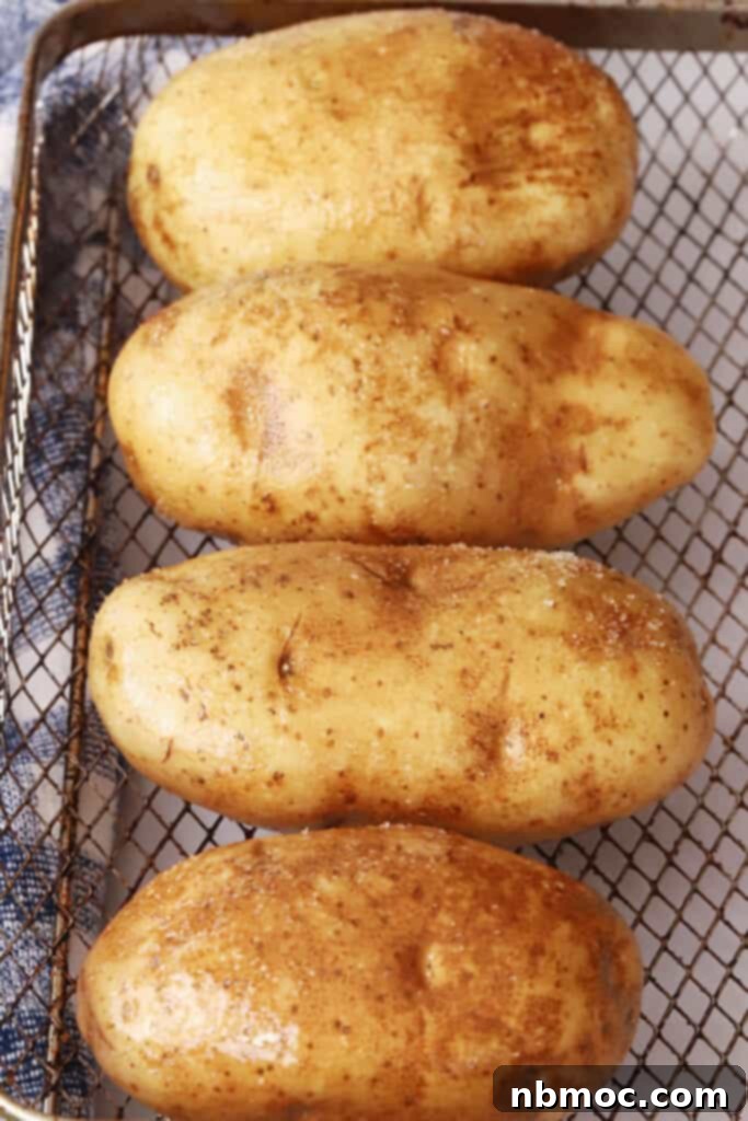 Crispy Fluffy Air Fryer Baked Potatoes 3 Uncooked russet potatoes prepared for air frying, resting in an air fryer basket, illustrating the initial steps of the air fryer baked potato recipe.