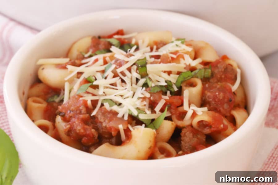 Grandma's American Goulash 3 Close-up of Best American Goulash recipe with rich beef and macaroni, generously topped with shredded cheese and fresh basil, showing its delicious texture.