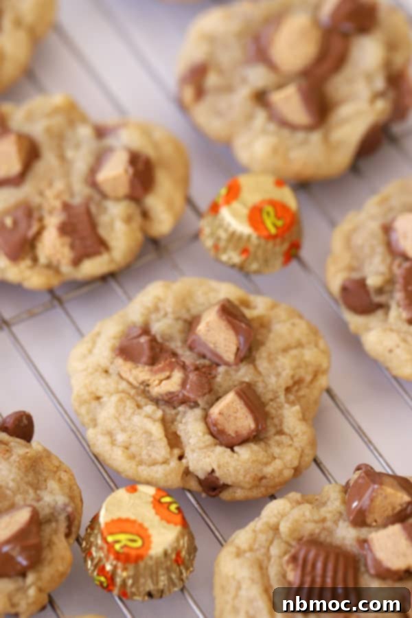 reese's peanut butter cookies on a rack with large chunks of candies baked into them.