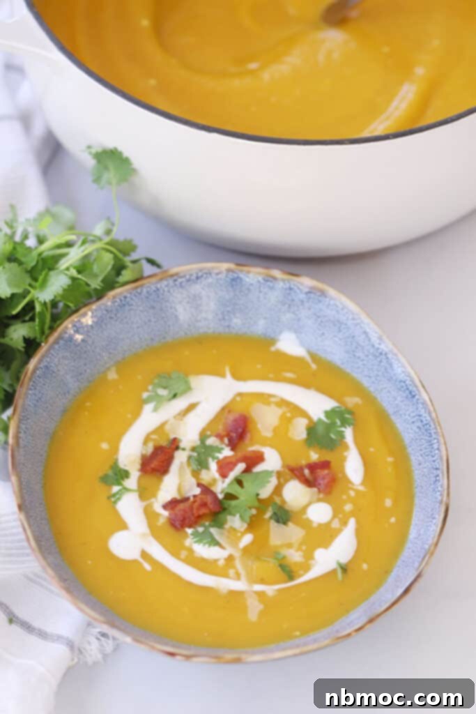 A soup bowl full of this acorn squash soup recipe topped with sour cream and bacon.