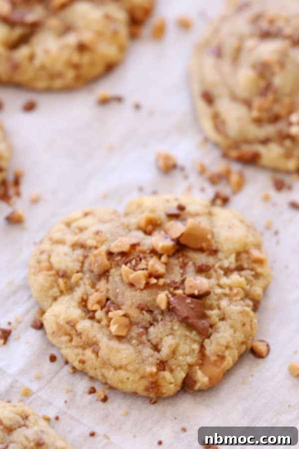 English Toffee Crunch Cookies 2 Close-up of freshly baked chocolate chip Heath toffee cookies on parchment paper, showcasing their golden edges and melt-in-your-mouth texture.