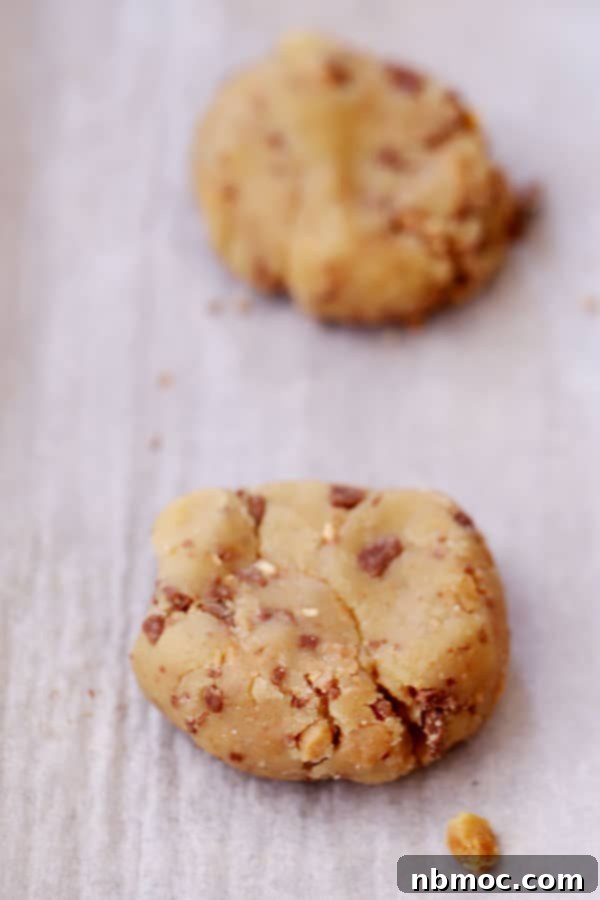 English Toffee Crunch Cookies 3 Scoops of Heath cookie dough with chocolate chips on a baking sheet lined with parchment paper, ready for baking.