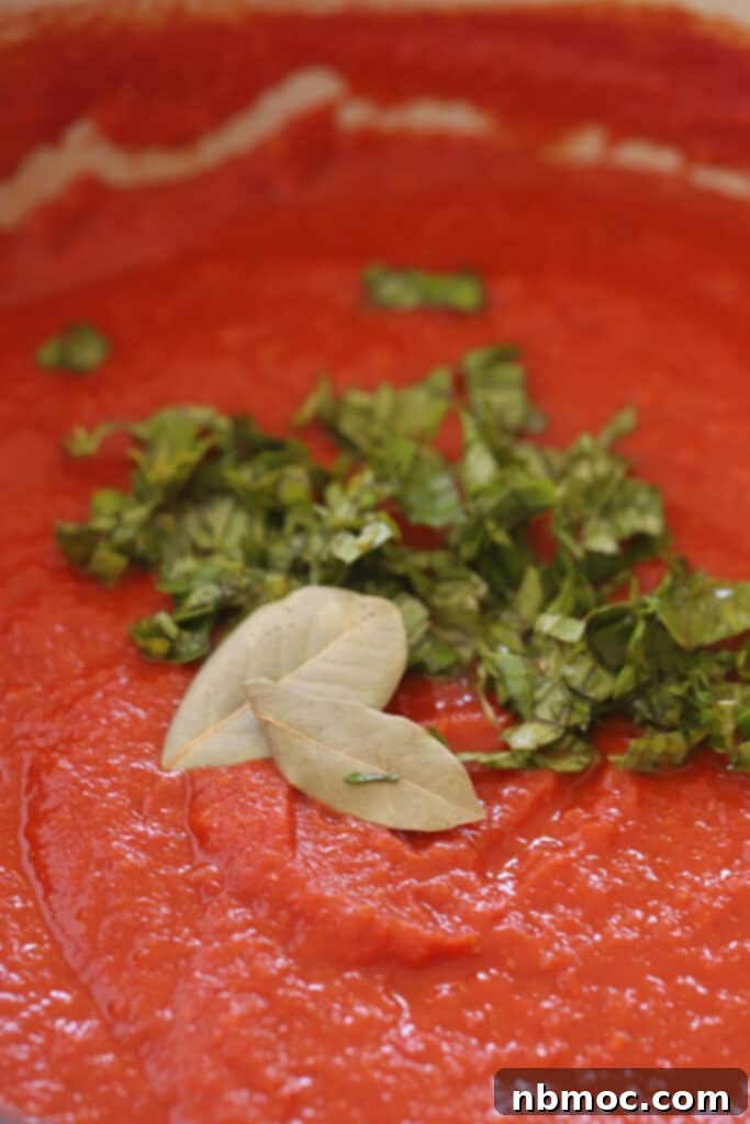 Slow Roasted Garden Tomato Marinara 9 Marinara sauce in a pot topped with fresh basil and bay leaves, signifying its fresh ingredients.