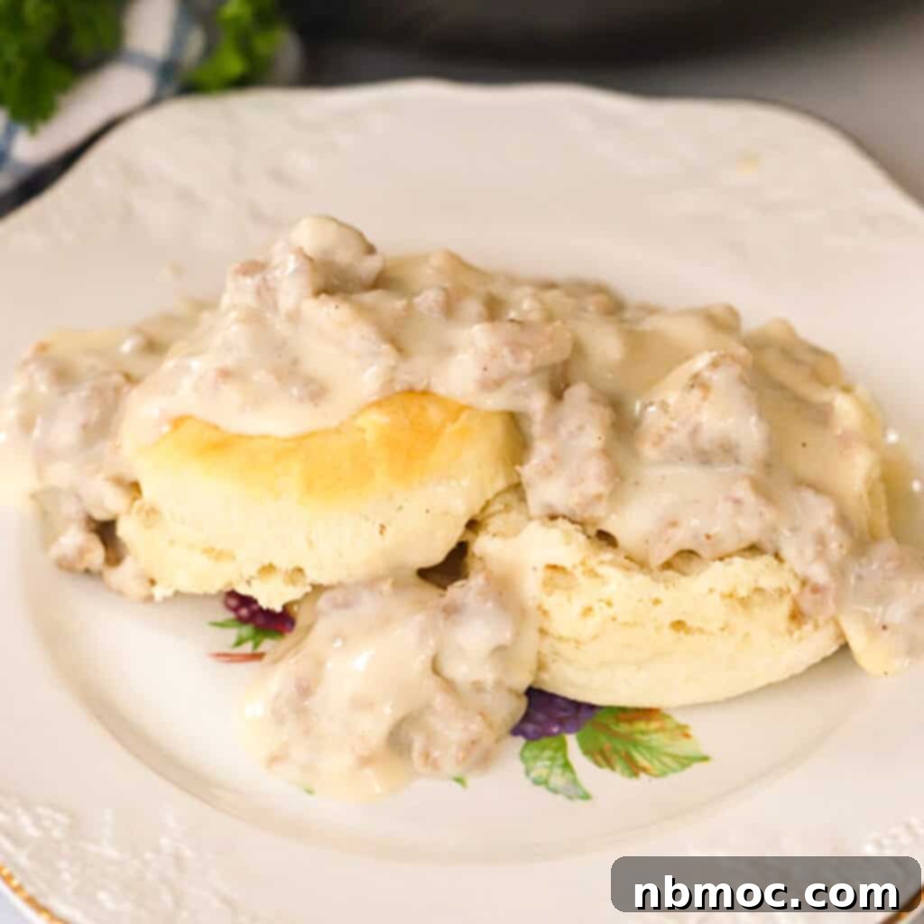Homemade sausage gravy generously spooned over biscuits on a decorative plate, garnished with fresh herbs.