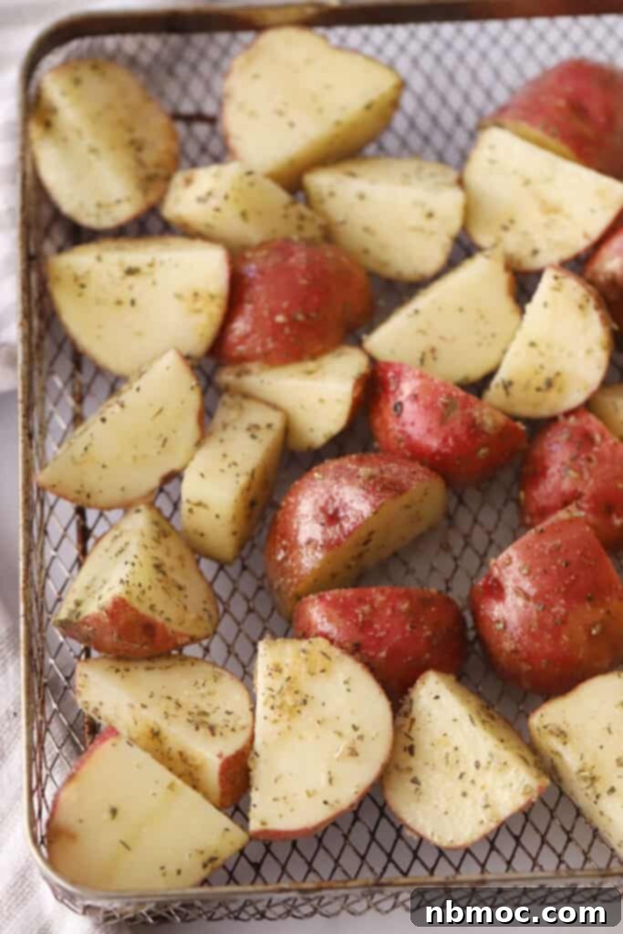 Crispy Air Fryer Red Potatoes 5 Quartered red potatoes covered in seasoning in an air fryer basket ready to cook.